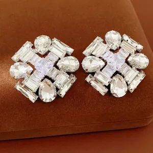 Close-up of oversized silver pin earrings with crystal teardrop and rhombus shapes