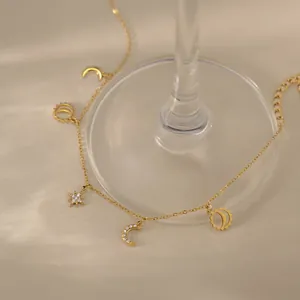 18k gold plated stainless steel anklet with sun, moon and star charms on a beige surface