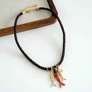 Detail view of a brown rope necklace with red and gold fish enamel pendants on white.