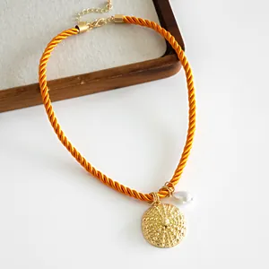 Close-up detail of a resort style orange rope necklace with gold textured pendant and pearl