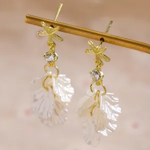 Detailed macro view of gold starfish earrings with white shell petal tassels