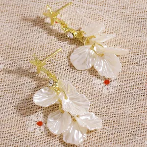 Close-up detail of gold starfish earrings with shimmering white shell petal tassels