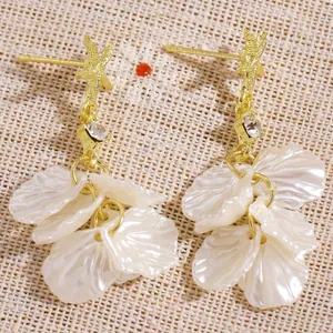 Close-up of gold starfish earrings with iridescent shell petal tassels and crystals.