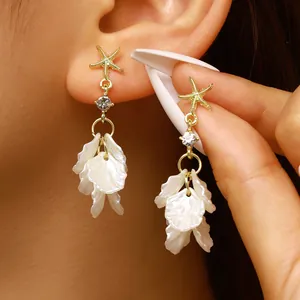 Macro close-up detail of starfish and white petal tassel earrings worn on a model's ear