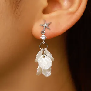Close-up detail of elegant silver starfish and white shell petal tassel earrings.