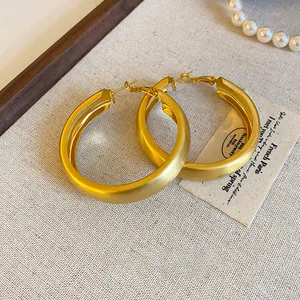 Close-up of minimalist brushed gold hoop earrings with silver needles on a textured surface.