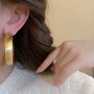 Detailed macro view of minimalist matte brushed gold hoop earrings worn on a model ear