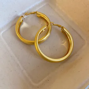 Close-up macro view of minimalist brushed gold hoop earrings with premium textured finish