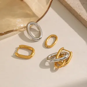 Detailed macro view of gold and silver U-shaped stainless steel earrings on textured beige background