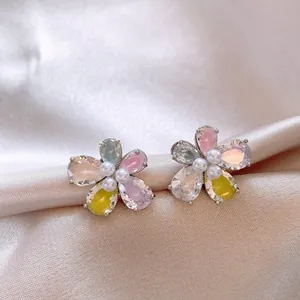 Primo piano di eleganti orecchini a fiore con zirconi colorati e perle su seta