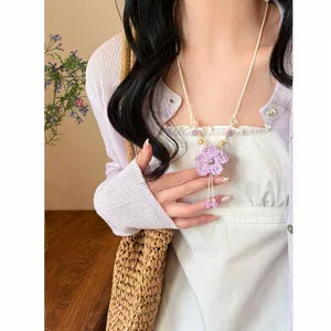 Detailed view of a purple hand-crocheted flower necklace on a model wearing a white dress.