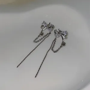 Close-up detail of silver-tone bow ear clips featuring sparkling gems and hanging tassels