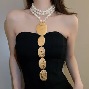 Détail d'un collier de perles exagéré avec des pendentifs ovales dorés martelés.