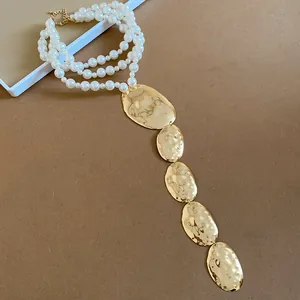 Détail du collier de perles à plusieurs rangs avec cinq pendentifs ovales dorés martelés.