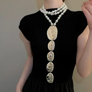 Détail d'un collier de perles à plusieurs rangs avec pendentifs ovales en métal sur modèle.