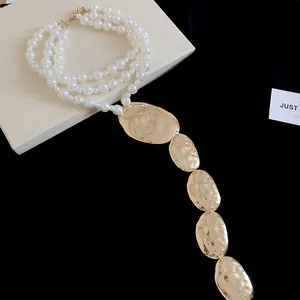 Détail d'un collier de perles à plusieurs rangs avec pendentifs ovales dorés martelés