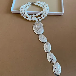 Détail d'un collier de perles à plusieurs rangs avec pendentifs ovales en argent martelé