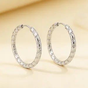 Close-up detail of silver-colored textured stainless steel hoop earrings with wave pattern