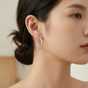 Detail of textured silver-colored stainless steel hoop earring worn on model's ear
