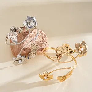 Dettaglio di eleganti bracciali da braccio in oro e argento con fiori di perle e farfalle.