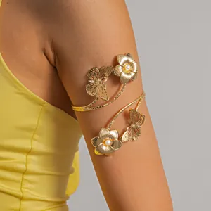 Dettaglio di un bracciale da braccio dorato con farfalle, fiori e perle su modella.