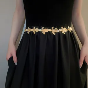 Detailed view of an elegant gold metal flower waist chain worn over a stylish black dress