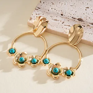Vue détaillée de créoles dorées ornées de fleurs et de pierres turquoise polies.