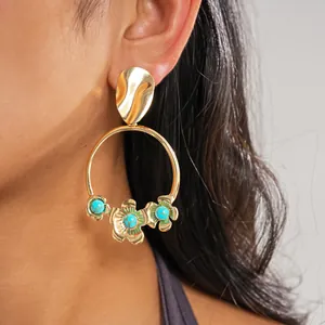 Gros plan de boucles d'oreilles créoles dorées avec fleurs et perles turquoises sur le modèle