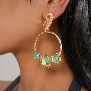 Gros plan d'une boucle d'oreille créole dorée avec des fleurs turquoise portée par un modèle