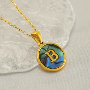 Gros plan d'un collier en acier inoxydable doré avec pendentif rond et lettre B sur nacre.