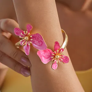 Gedetailleerde close-up van levendige roze emaille bloemen op een gouden gedraaide armring