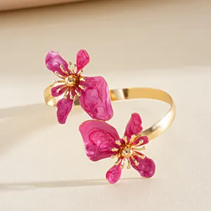 Close-up detail van een gouden gedraaide armband met twee levendige roze emaille bloemen.