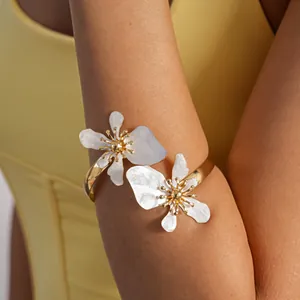 Gedetailleerd macrozicht van een gouden armmanchet met witte geëmailleerde bloemen.