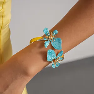 Detailweergave van een goudkleurige armband met twee lichtblauwe geëmailleerde bloemen