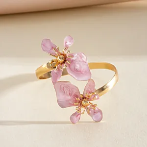 Elegant roze emaille bloemendetail op een goudkleurige gedraaide metalen armband