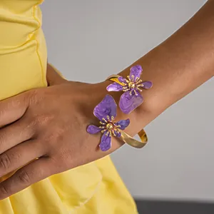 Elegante goudvergulde armband met paarse emaille bloemen op de arm van een model