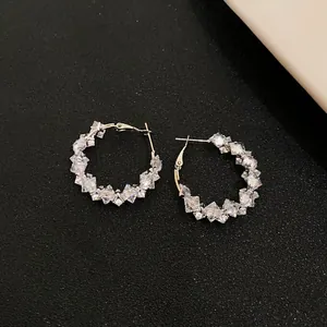 Macro view of exquisite zircon hoop earrings resting on a textured black surface.