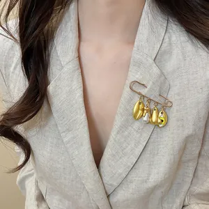 Detail shot of a unique gold metal brooch with artistic charms on a linen blazer.