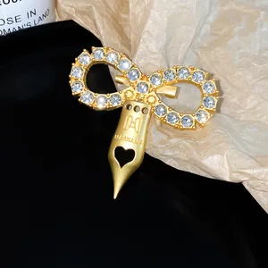 Detail view of a gold-toned bow brooch with zircons and a fountain pen nib pendant