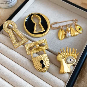 Detailed shot of surrealist gold brooches with eye and keyhole designs in an elegant tray.