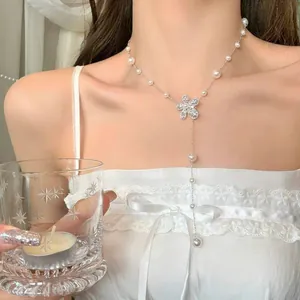 Dettaglio macro che mostra il ciondolo a fiore d'argento e le perle di una collana a Y