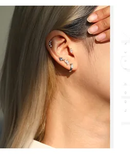 Close-up detail of multiple S925 sterling silver moissanite stud earrings on ear.