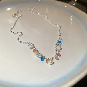 Detailed close-up of elegant rainbow zircon and pearl necklace on a white ceramic plate