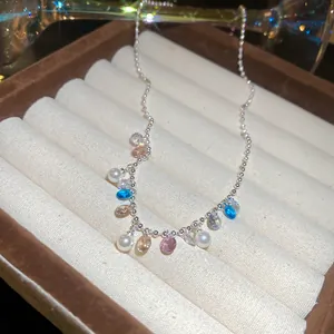 Close-up of a silver ball chain necklace with colorful zircons and white pearls.