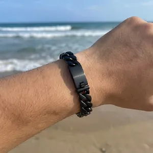 Macro view of men's matte black Cuban link bracelet with engravable metal tag on wrist