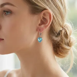 Nahaufnahme eines Models mit hellblauen herzförmigen Kristallohrringen aus Edelstahl