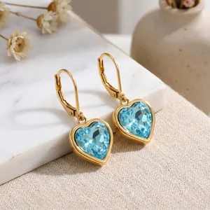 Nahaufnahme von blauen herzförmigen Kristallohrringen mit goldenem Edelstahlrahmen