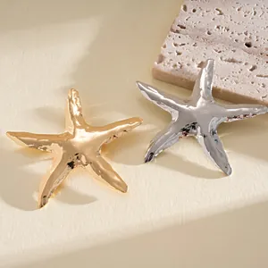 Dettaglio delle spille a forma di stella marina in oro e argento con finitura in metallo stropicciato.