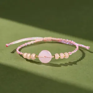 Primo piano di bracciale intrecciato rosa fatto a mano con calcedonio tondo e perline oro