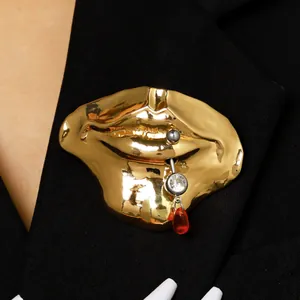 Detailaufnahme einer surrealistischen goldenen Lippenbrosche mit Piercing und Kristall